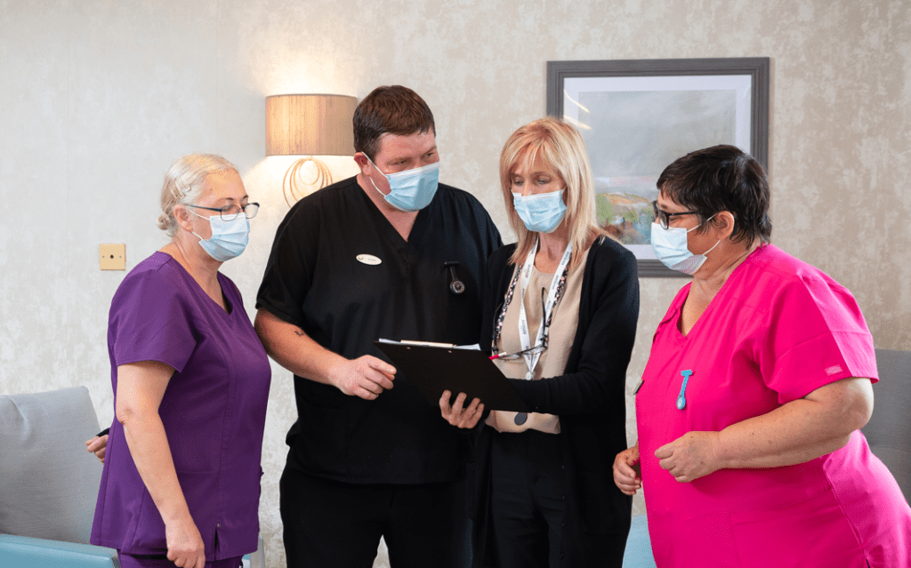 Four people stood in care home having a meeting wearing face masks