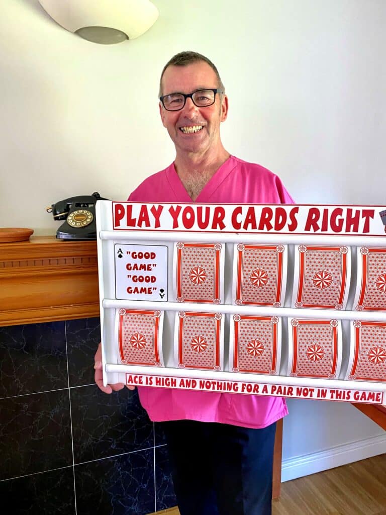 Andy stands in pink tunic with giant playing cards