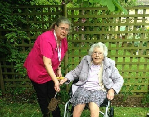 Woman in pink tunic helps older woman in wheelchair in garden