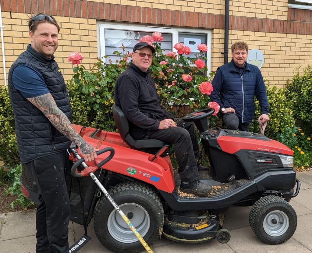 Three men with gardening tools outside care home